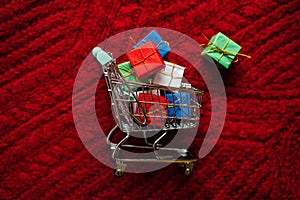 Christmas xmas early sale shopping concept. Shopping cart with many gift boxes on red knitting background