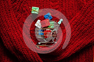 Christmas xmas early sale shopping concept. Shopping cart with many gift boxes on red knitting background