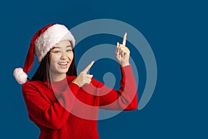 Christmas, xmas Happy woman in santa claus hat pointing finger at copy space on blue background, smiles