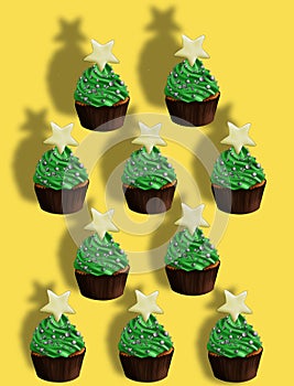 Christmas yellow background pattern of green cupcakes in the shape of a holiday tree with a star on top and sprinkles.