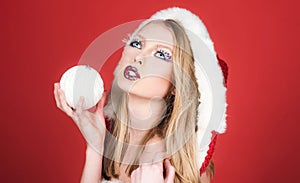 Christmastime. Sexy Santa Claus girl with white Christmas ball in hand. Winter holidays celebration. Beautiful blonde