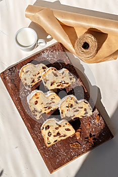 Christstollen, stollen sliced on pieces on wooden board, cup with milk on beige table background with sunlight shadow