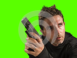 Chroma key green background action portrait of serious and attractive hitman or special agent man holding gun pointing the handgun