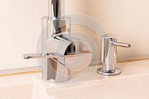 Chrome faucet and liquid soap dispenser in modern kitchen with granite sink