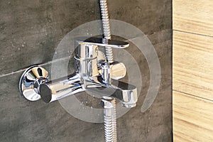 Chrome metal faucet for hot and cold water, with a shower hose, mounted in a wall covered with gray tile imitating concrete