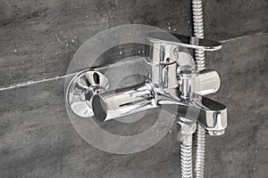 Chrome metal faucet for hot and cold water, with a shower hose, mounted in a wall covered with gray tile imitating concrete