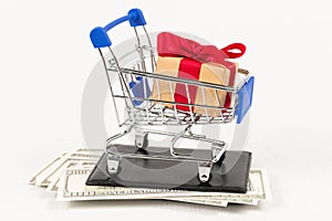 Chrome shiny shopping trolley on wheels with gift box on wallet with dollars on white background. selective focus