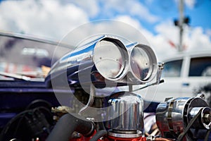 A chrome supercharger on an old car, against the sky.