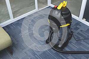 A chrome upright vacuum cleaner placed on the carpeted flooring at the corner of an office space