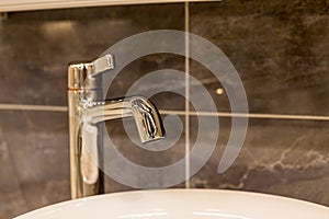 Chrome water faucet with marble counter tops and a white sink.Luxury faucet mixer in a beautiful gray bathroom. Sanitary