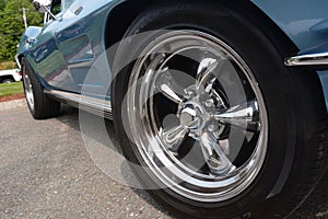 Chrome wheels gleam brightly on a blue sportscar under a sunny early summer day.