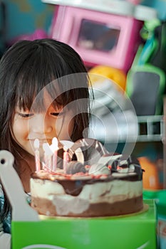 Chubby Asian little girl celebrating her birthday at home. Happy and jovial in front of the cake. Soft focus