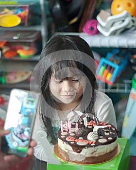 Chubby Asian little girl celebrating her birthday at home. Happy and jovial in front of the cake. Soft focus