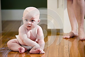 Chubby baby sitting on floor wearing diaper photo