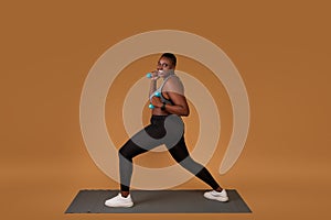 Chubby black exercising with dumbbells on yoga mat