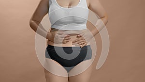 Chubby caucasian female in underwear appreciate her forms and show thumbs up with both hands. Beige studio background