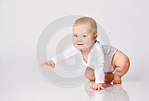 Chubby ginger little one in bodysuit, barefoot. He is sitting on floor isolated on white studio background. Close up, copy space