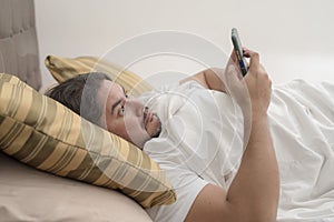 A chubby man in his 30s is shocked by a controversial social media post on his cellphone while lying on the bed photo