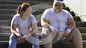 Chubby man and woman resting after hard workout on stairs, breathing heavily
