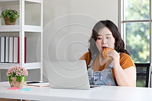 Chubby woman eating a hamburger while working from home