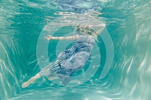 Chubby woman in grey evening long dress swimming underwater on her holidays and enjoy with relax