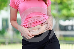 Chubby woman hand holding her own belly fat at outdoor.