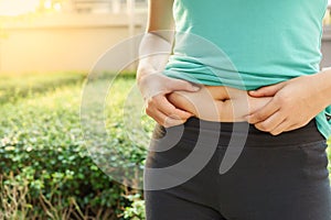 Chubby woman hand holding her own belly fat at outdoor under the