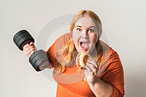 Chubby woman sport at home standing isolated on white holding dumbbell eating burger cheerful