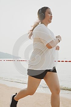 chubby woman wearing sport wear and haedphone running on sea beach with happiness