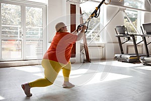 Chubby woman working in bodyweight training program using trx loops