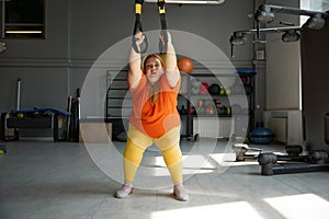 Chubby woman working in bodyweight training program using trx loops