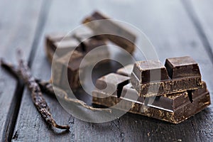 Chunks of dark chocolate bar and vanilla beans on wooden table