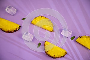 chunks of fresh pineapple accompanied by mint and ice bubbles on a violet background with palm tree shade photo