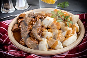 Chunky beef stew with savory sauce beside potato dumplings.