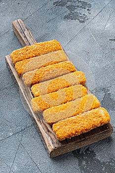 Chunky breaded frozen fish fingers, on wooden cutting board, on gray background