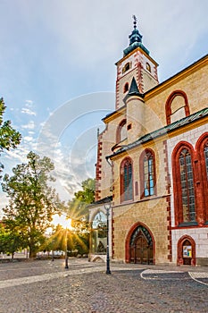 Kostol Nanebovzatia pri západe slnka so slnečnými lúčmi presvitajúcimi cez stromy. Banská Bystrica, Slovakia.