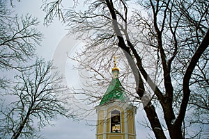Church bell tower against the sky, bare dark branches of trees on a cold winter day