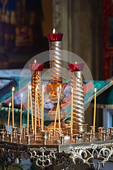 Church candles are burning on a large golden vintage candlestick in the orthodox church. Christian faith and traditions. Theme of