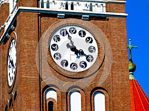 church clock tower closeup detail with black hands. white clock face. brick tower facade