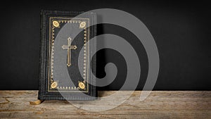 Church faith Christian background - Old holy bible with golden cross on old rustic vintage wooden table and black wall