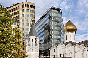 Church next to modern houses against the blue sky on a sunny day. Contrast of architecture