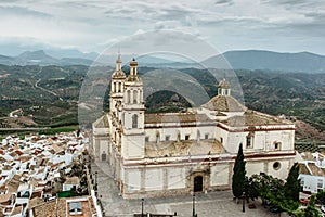 Church of Our Lady of Incarnation in Olvera, Andalusia, Spain. View of the church and green fields with mountains in background.