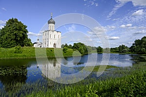 The church of Pokrova-na-Nerli and its reflection in the river among trees and meadows in Bogolyubovo, Russia