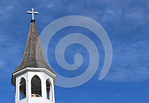 Church roof with metal cross on top and white bell tower with fluffy clouds