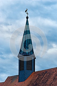 Church spire with stork standing high up on cross