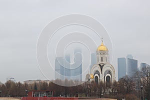 Church of St. George the Victorious on Poklonnaya Gora against the background of skyscrapers Moscow city in the fog, Russia