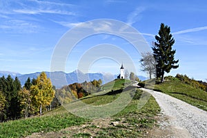 The church of St. Primoz in Slovenia near Jamnik with colorful autumn trees and blue sky