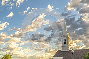 Church steeple and roof viewed against blue sky and puffy clouds on a sunny day