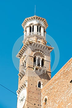 Church tower in Verona made of stone, a clock, with several ledges on a blue sky background