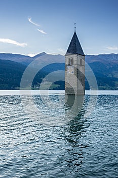 Church under water, drowned village, mountains landscape and peaks in background. Reschensee Lake Reschen Lago di Resia.